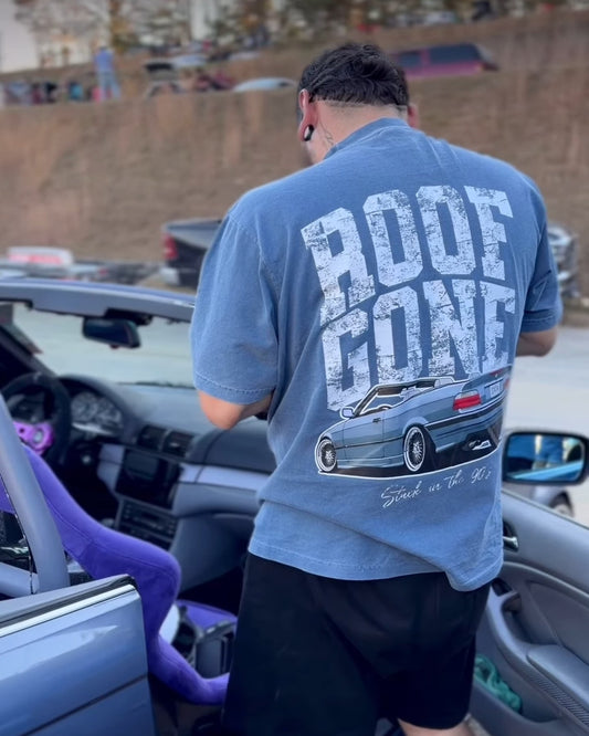Person wearing a blue t-shirt with 'ROOF GONE' text and car graphic, standing next to a vehicle.